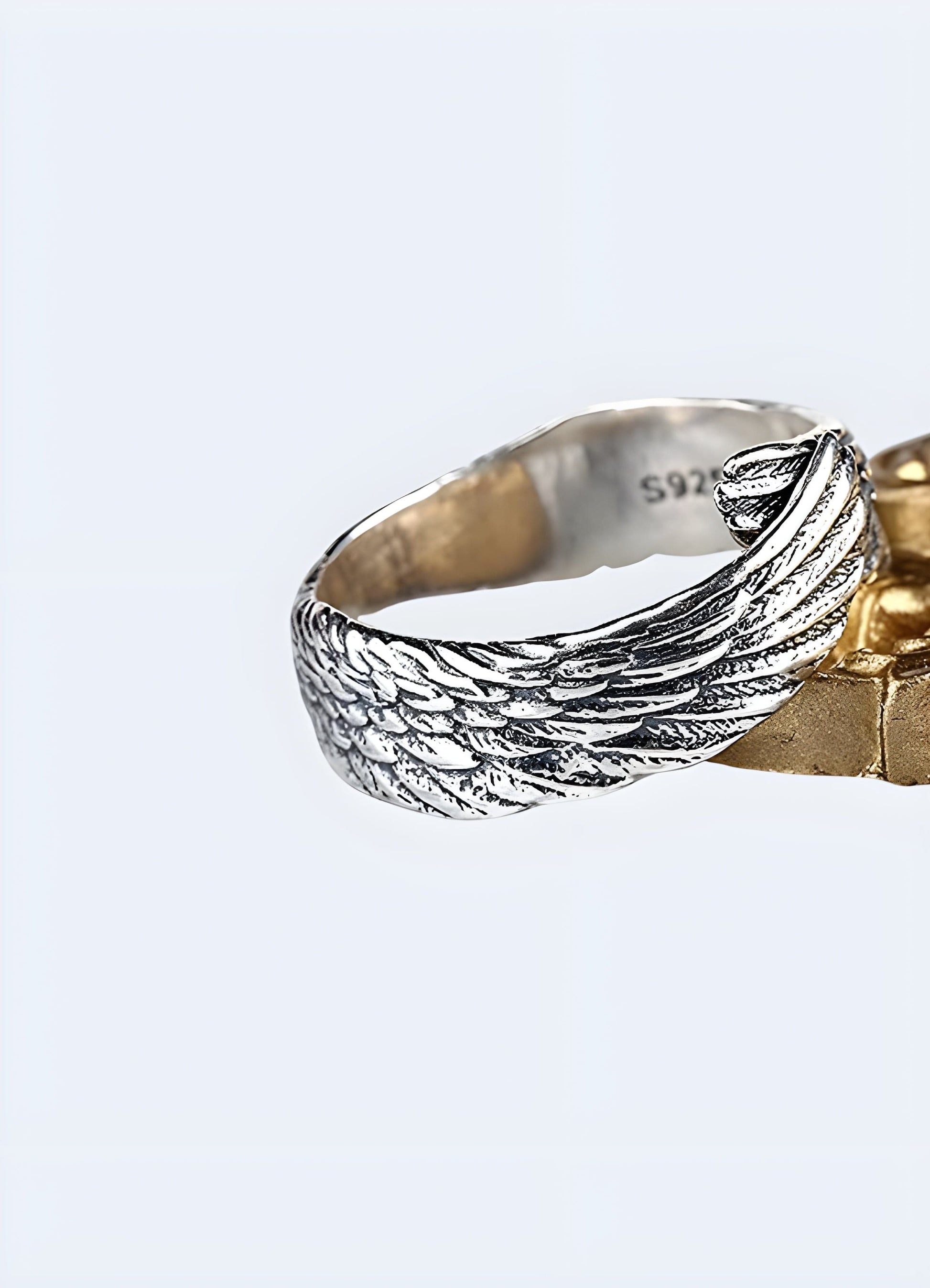 The ring features a delicate design with intricately carved feather details that wrap around the finger