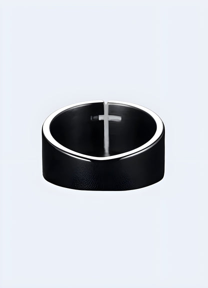 Detailed view of the back side of a black cross ring, showcasing its smooth finish and minimalist design against a blurred backdrop.