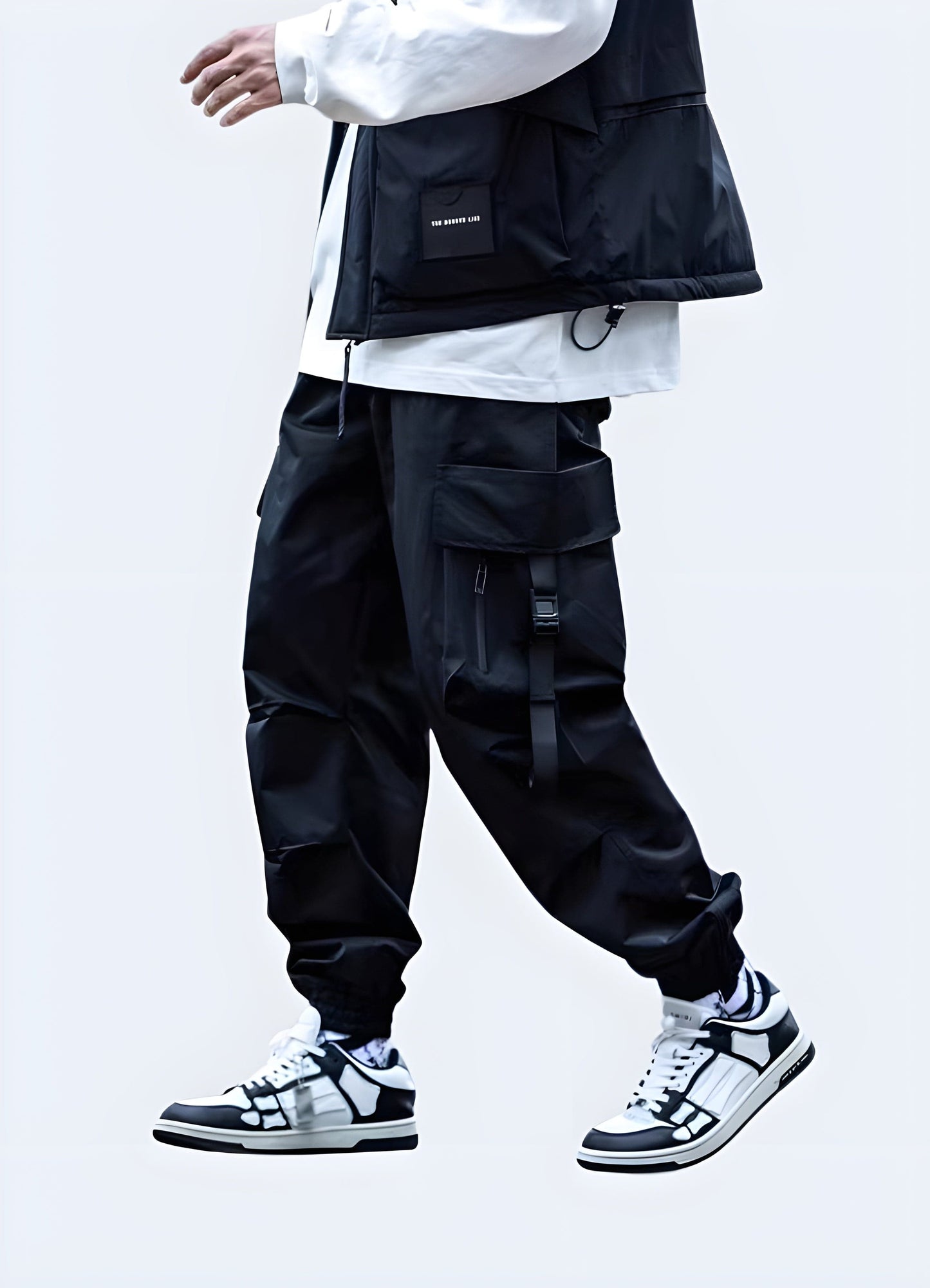 Man wearing black Japanese techwear cargo pants with multiple pockets and straps, front view, UK style.