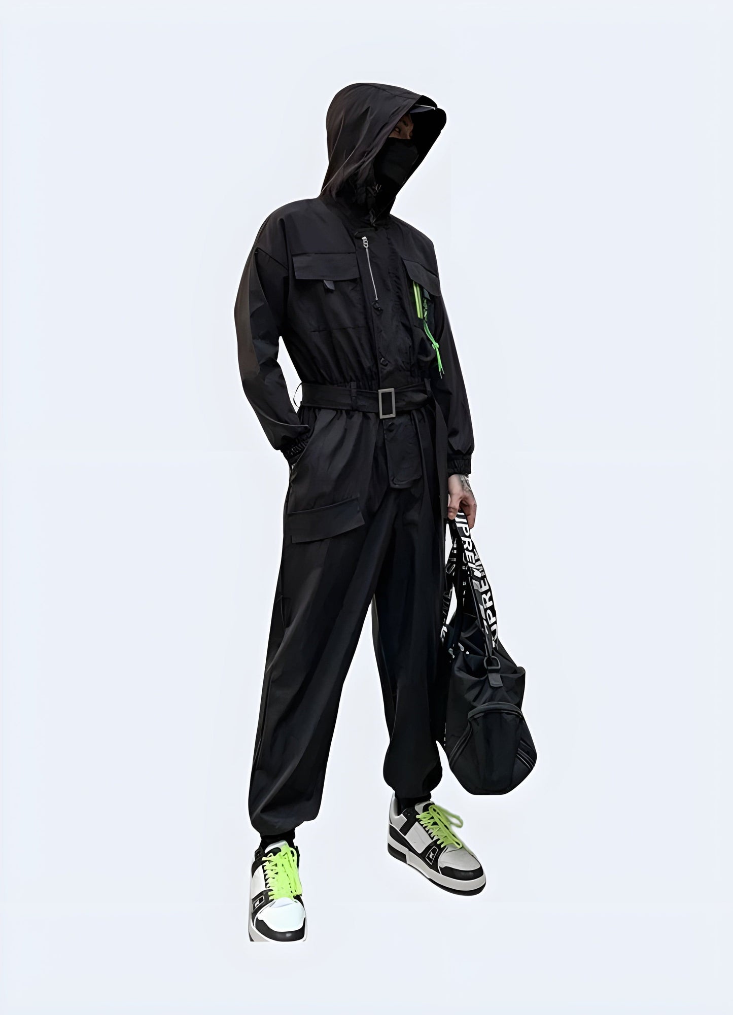 Side view of a man wearing a sleek black techwear jumpsuit with hood, showcasing the garment's unique design and functionality in an urban UK environment.