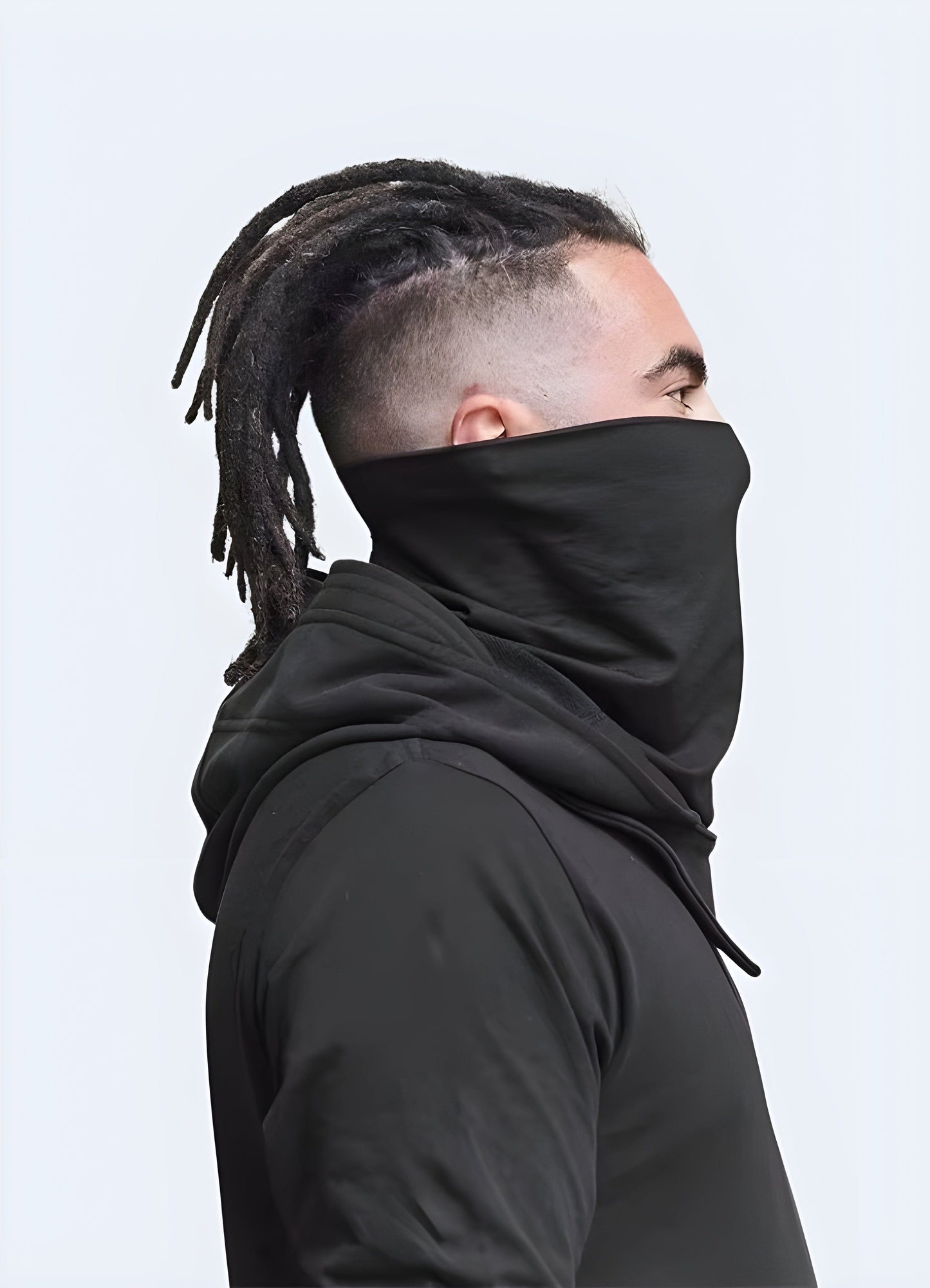 Man wearing a fashionable black techwear hood with a futuristic design, showcasing a side view of the garment in a UK setting.