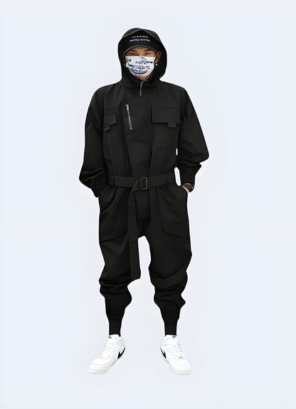 Futuristic black techwear jumpsuit with multiple pockets and straps, worn by a model in an urban setting in the UK.