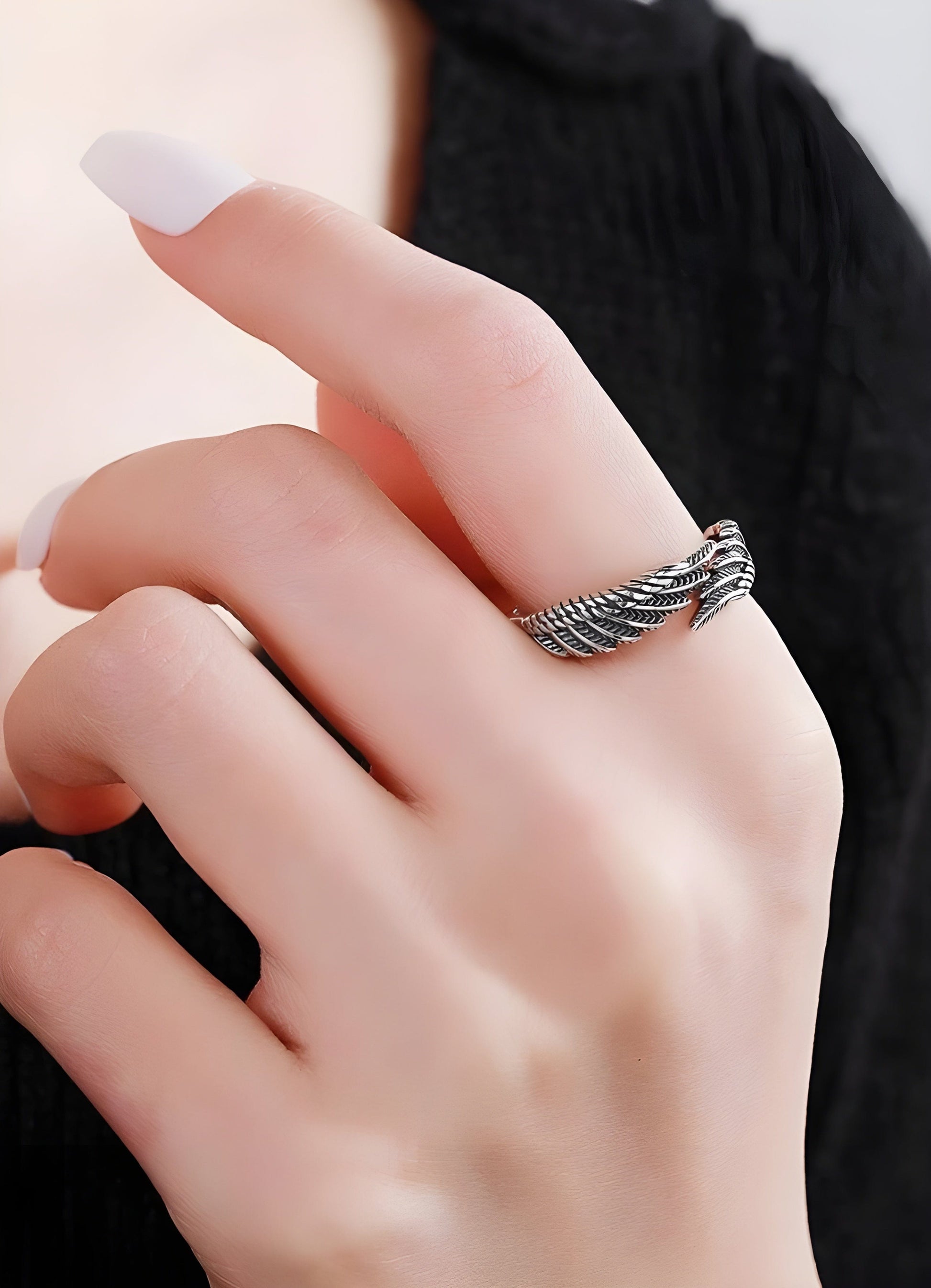 Person wearing an angel feather ring in the UK, front side view. The ring features intricately carved feather details that wrap gracefully around the finger.